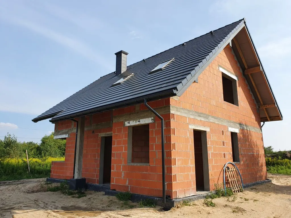 Dom z poddaszem w stanie surowym otwartym - ściany z pustaków ceramicznych, dach dwuspadowy z dachówką, puste otwory okienne