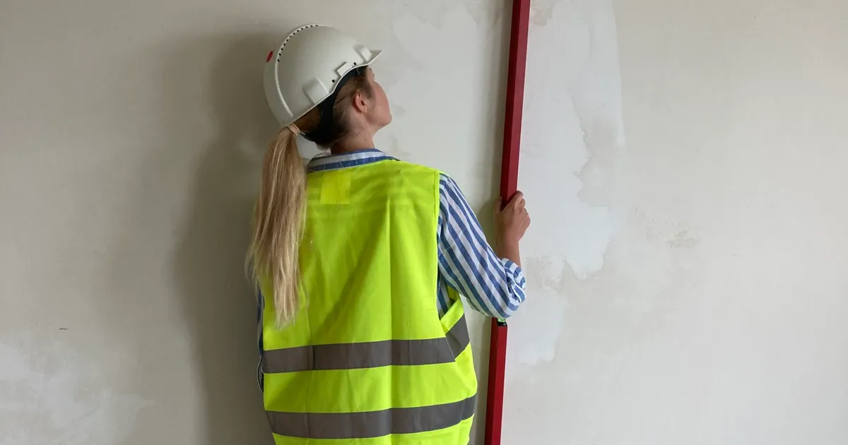Inspektor nadzoru sprawdza tynki poziomicą podczas odbioru technicznego mieszkania od dewelopera