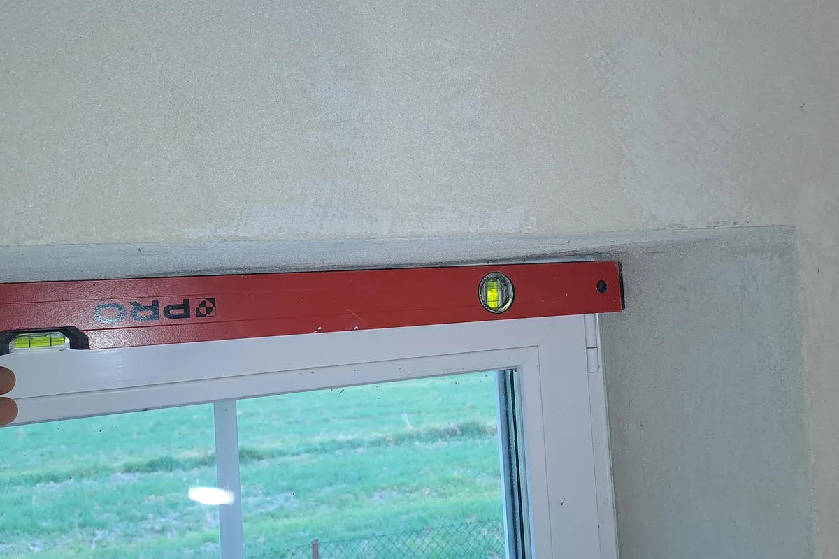 Pomiar płaszczyzny tynków łatą kontrolną — widoczna szczelina przekraczająca normę 3 mm